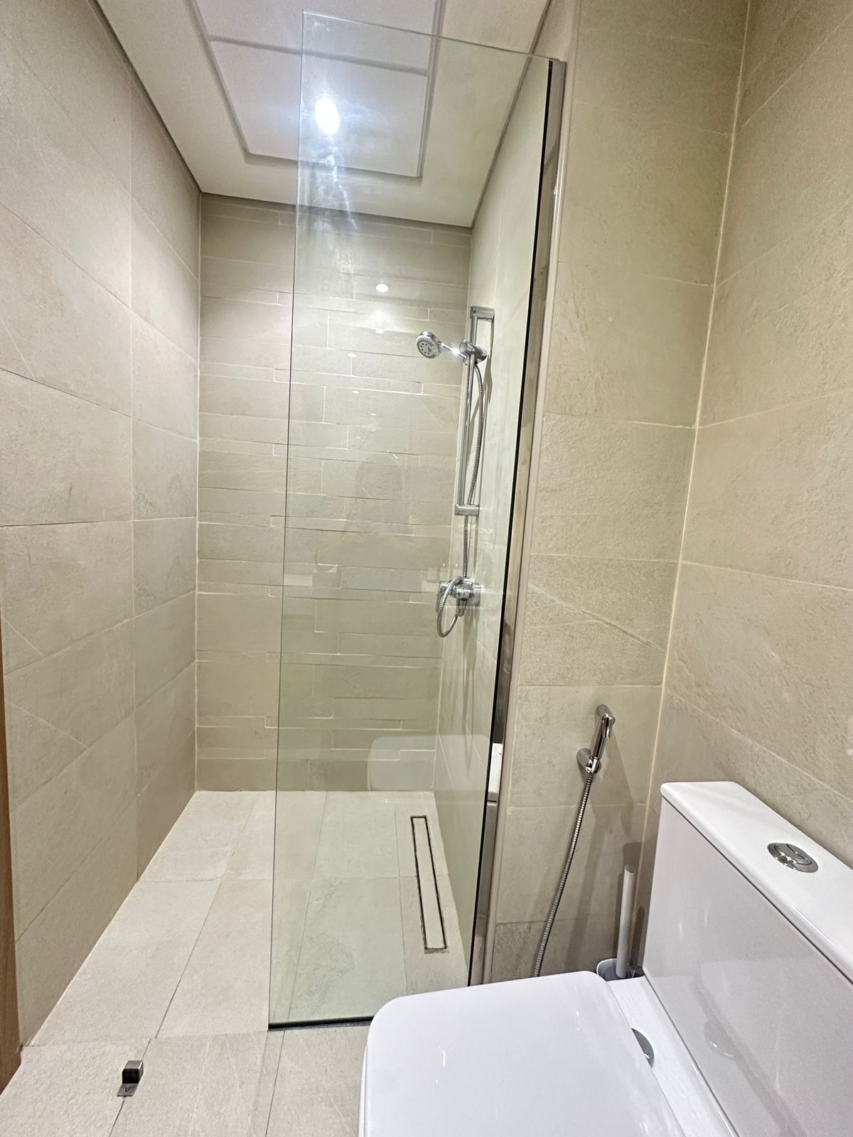 A modern bathroom with a glass-enclosed shower, a white bathtub, and beige tiled walls.