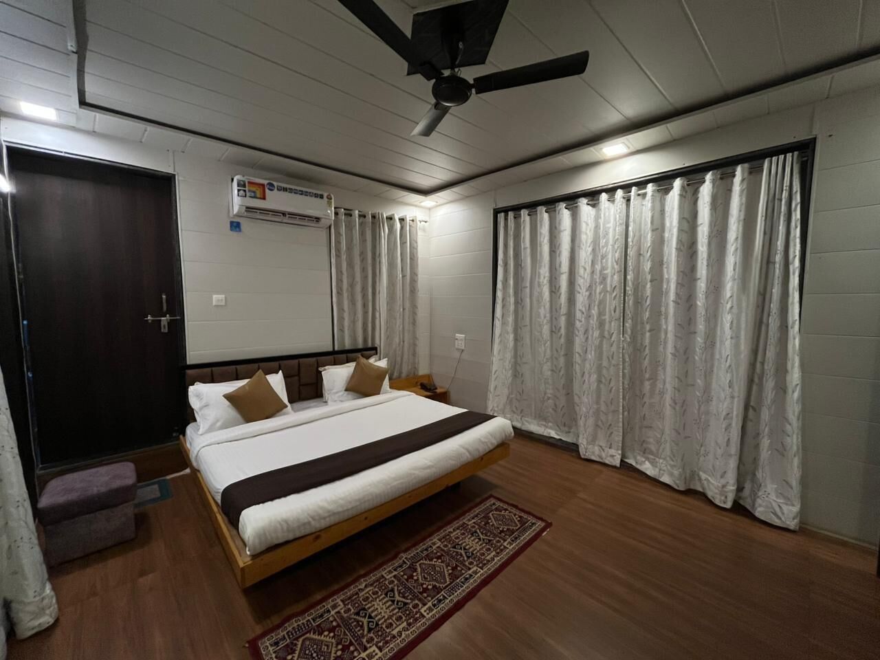 A bedroom with a bed, curtains, a ceiling fan, and a small table.