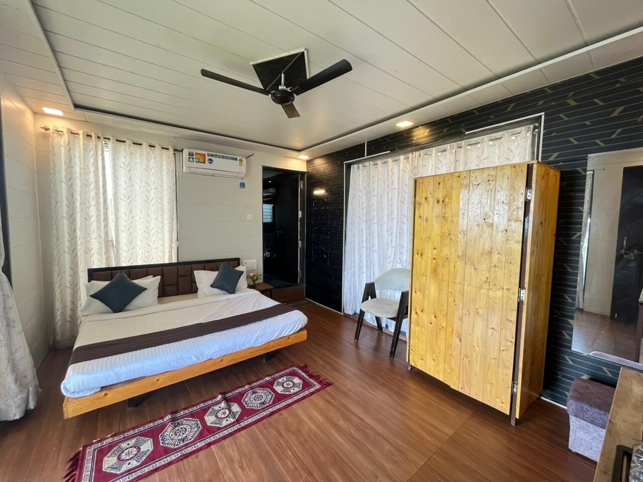 Une chambre à coucher avec un lit, un ventilateur de plafond, une armoire en bois et une petite chaise.