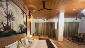 A spacious bedroom with a large bed, multiple seating areas, and ceiling fans. - Astoria Lagoon Resort (Igatpuri)