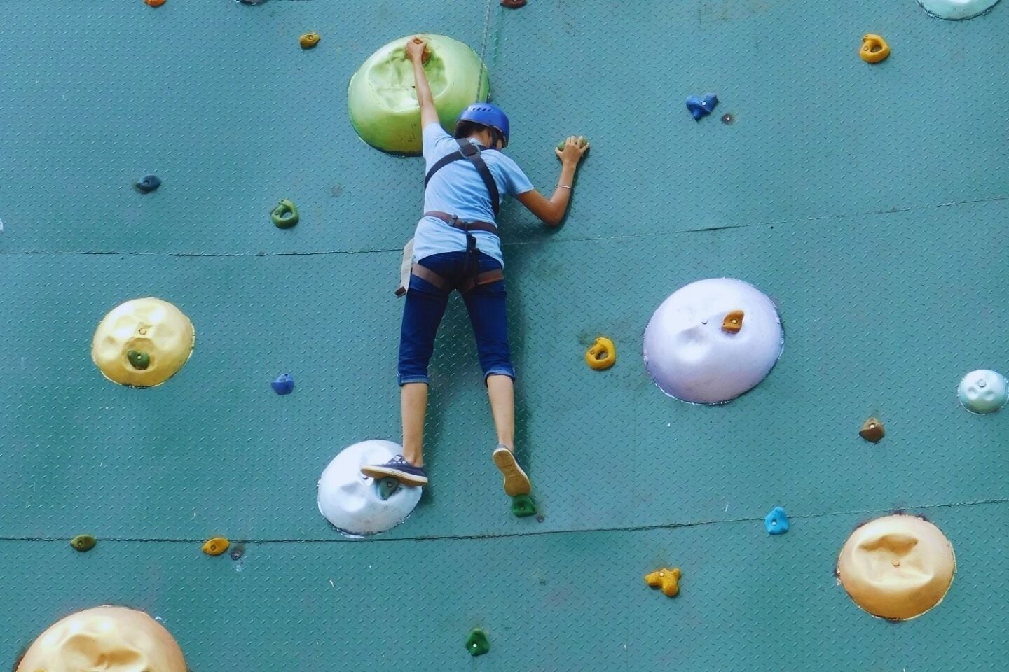 Una persona escalando una pared de escalada con diferentes puntos de agarre.
