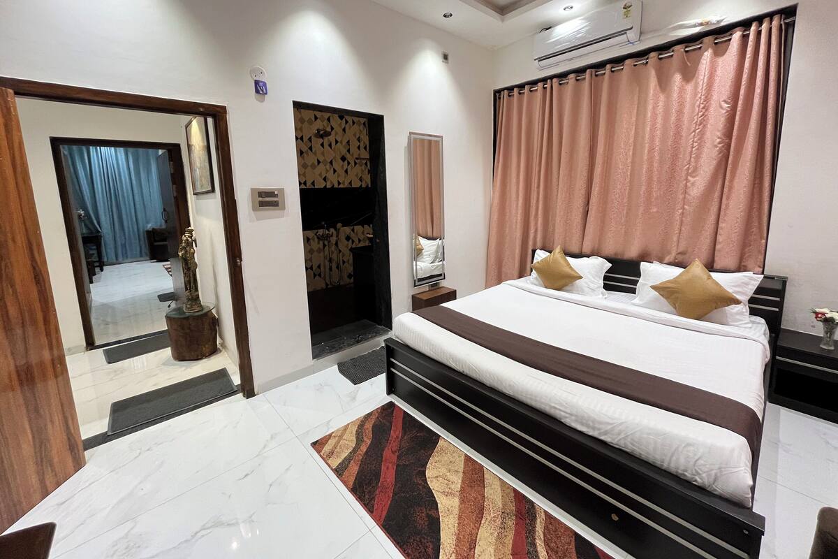 A modern hotel room with a large bed, a bathroom with a shower, and a small table with a vase.