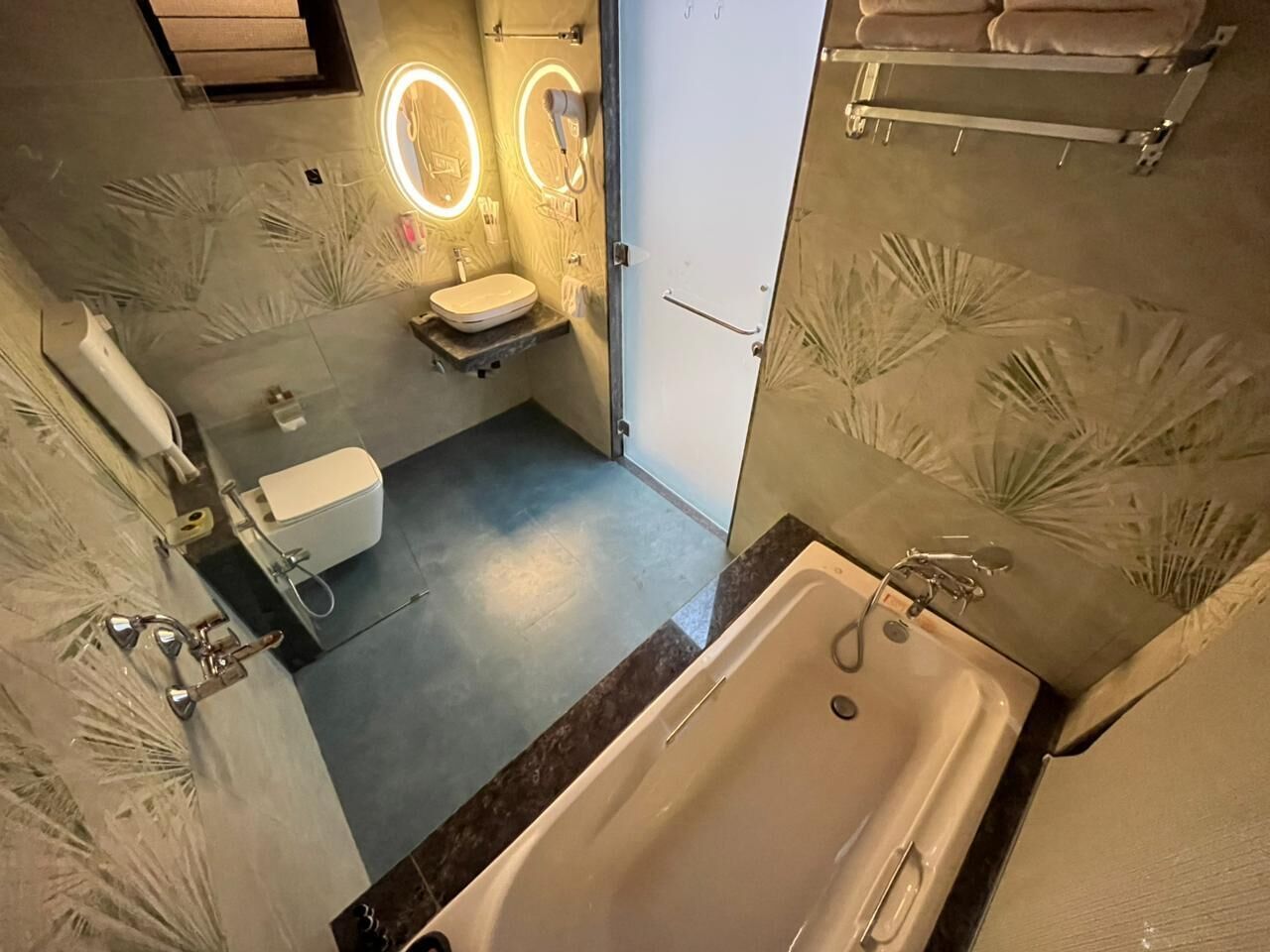 A bathroom with a bathtub, toilet, and sink, featuring a modern design with patterned walls and built-in lighting.