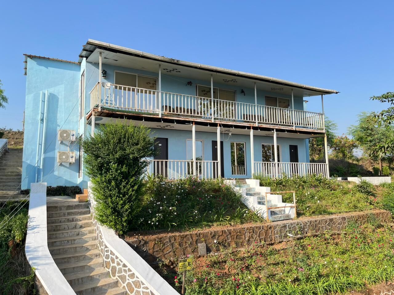 A two-story building with a balcony, surrounded by greenery and a stone wall.