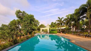 A clear blue pool surrounded by lush greenery and a gazebo in the background. - Astoria Lagoon Resort (Igatpuri)