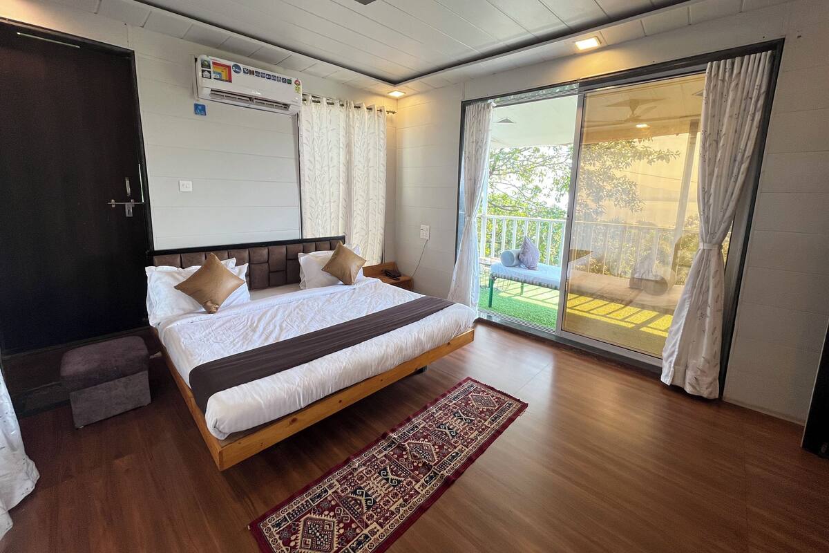 A bedroom with a large bed, a wooden floor, a ceiling fan, and a view of a balcony.