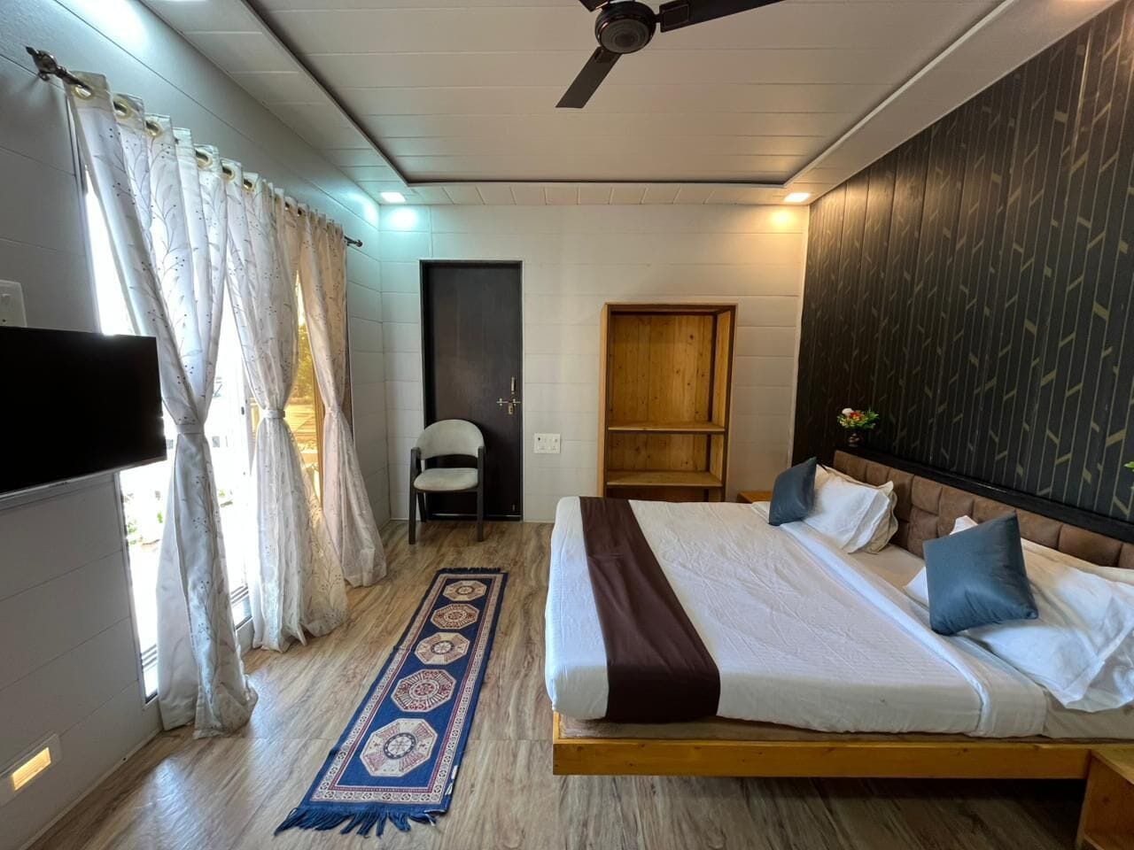 A bedroom with a bed, a chair, a wooden wardrobe, and a ceiling fan.