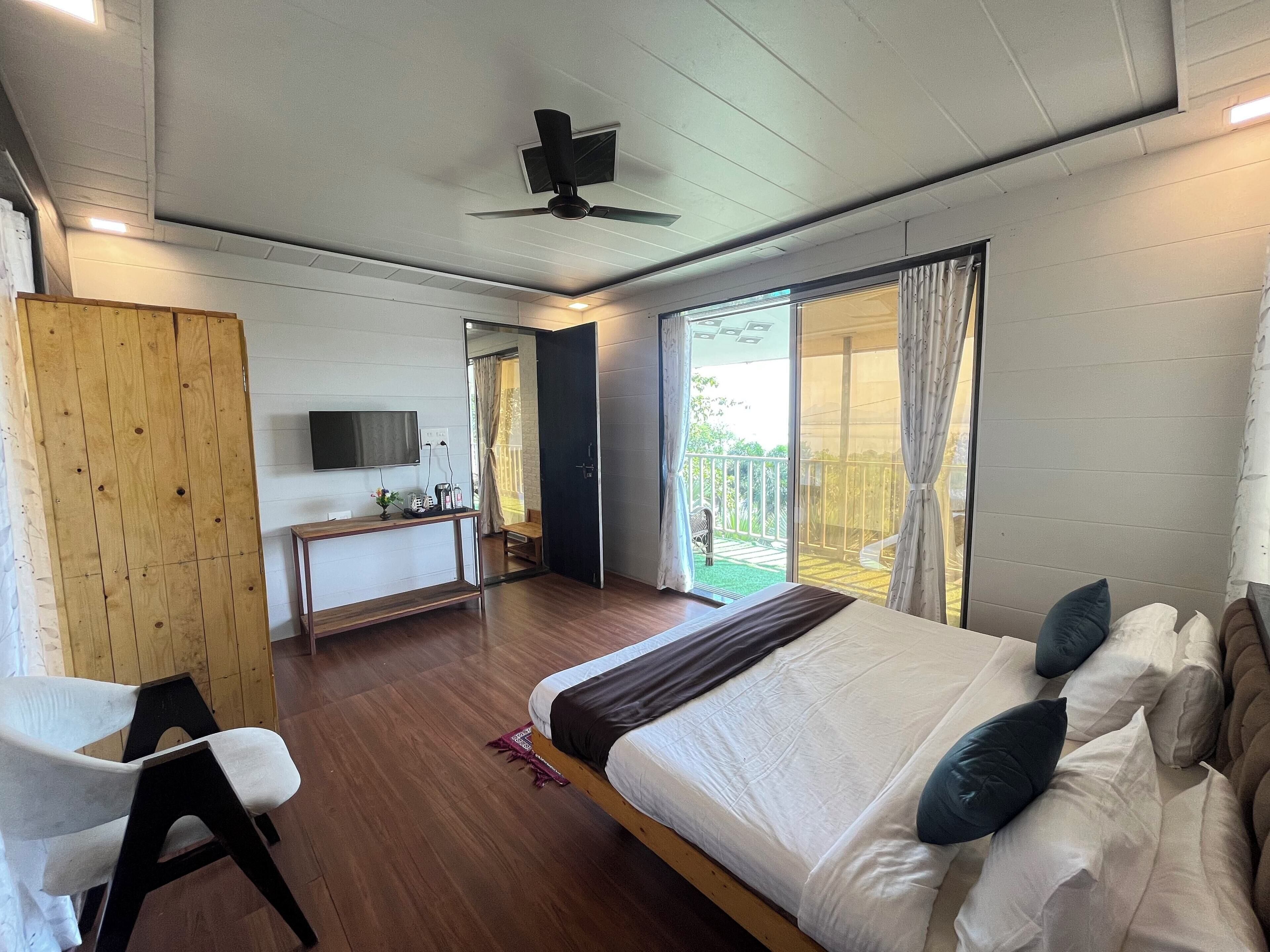 Une chambre à coucher comprenant un lit, un bureau, une chaise, un téléviseur et un balcon avec des rideaux.