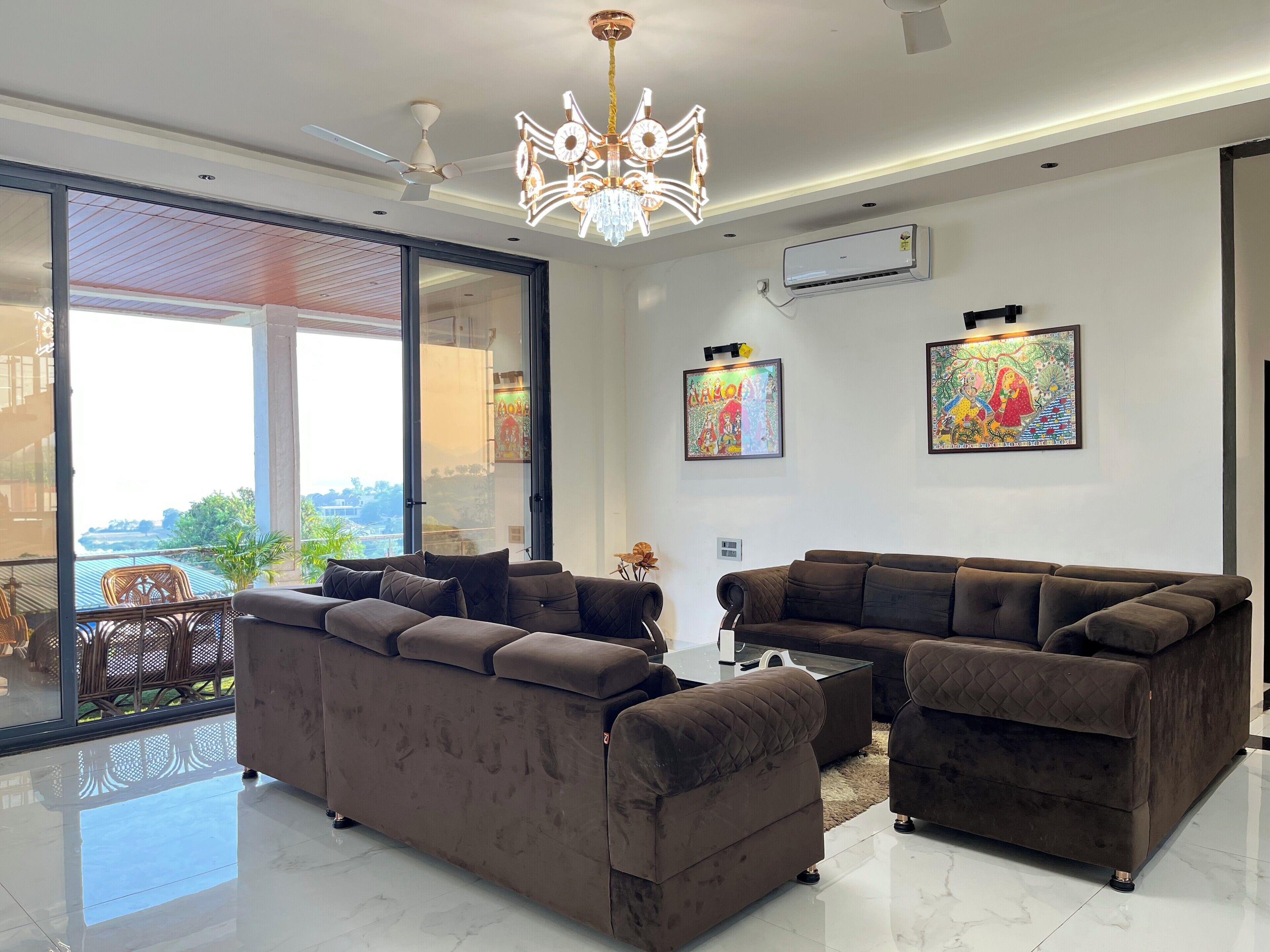 A modern living room with two brown sofas, a glass door leading to an outdoor area, and two framed artworks on the wall.