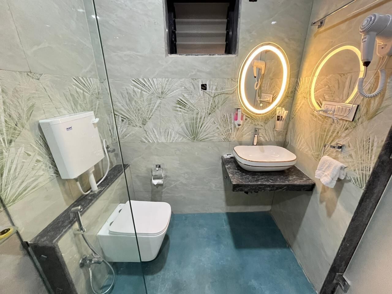 A modern bathroom with a glass partition, a white toilet, a sink with a marble countertop, and a hairdryer mounted on the wall.