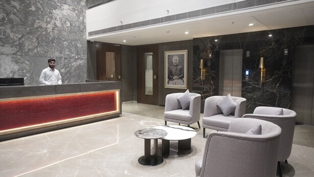 A modern lobby with a reception desk, seating area, marble flooring, and a large framed portrait on the wall.