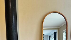 A living room with a wood-burning stove, a mirror reflecting the room, and a sofa. - Ruby’s Nest – A countryside experience (Te Poi)