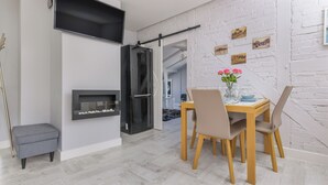 A modern dining area with a table set for two, a fireplace, and a TV mounted on the wall.