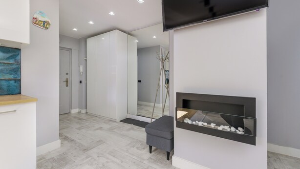 A modern interior with a flat-screen TV mounted on the wall, a minimalist fireplace with a stone shelf, and a door leading to another room.