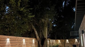 Una terraza de madera con un banco integrado y una pequeña mesa, rodeada por una valla de madera y árboles.