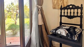 Una habitación con vistas a la vegetación exterior, una silla negra con un cojín estampado, una escultura en la pared y una puerta con cortina.