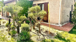 Un edificio con tejado de tejas, un sendero de ladrillo y diversos arbustos y árboles en primer plano.