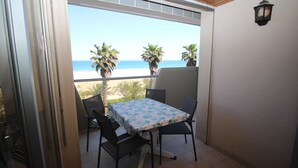 Un balcón con mesa y sillas, con vista a una playa con palmeras y el océano.