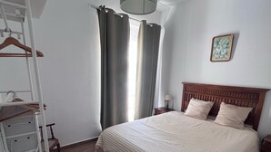 A bedroom with a bed, a wooden headboard, a hanging light fixture, a window with curtains, and a wall-mounted picture. - Apartment 2nd left (1 Bedroom) (Sevilla)