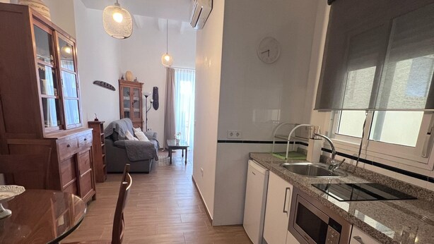 A modern kitchen with white cabinets, a granite countertop, and stainless steel appliances. There is a dining area with a wooden table and chairs. - Apartment 2nd left (1 Bedroom) (Sevilla)