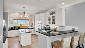 A modern kitchen with white cabinetry, a central island, and a large window providing natural light. - Vitamin Sea - 2779   “Ponte Vedra” (Ponte Vedra Beach)