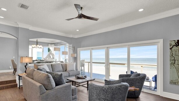 A spacious living room with a large window overlooking a beach, a ceiling fan, and a modern interior design. - Vitamin Sea - 2779   “Ponte Vedra” (Ponte Vedra Beach)