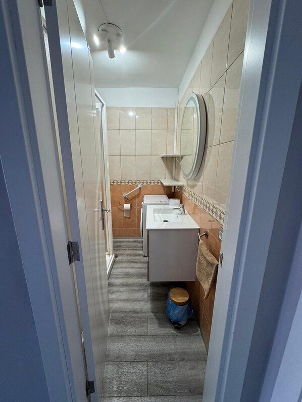 A narrow hallway leading to a bathroom with a sink, mirror, and toilet.