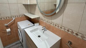 Ein Badezimmer mit Waschbecken, Spiegel, Handtuchhalter, Toilettenpapierhalter und einer Waschmaschine.