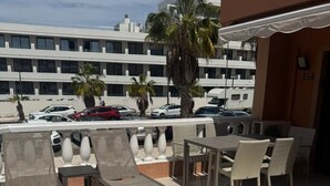 Ein Außenbereich mit Lounge-Möbeln und Tischen, einem Fliesenboden und Blick auf geparkte Autos sowie Gebäude im Hintergrund.