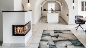 A modern kitchen with an island, a fireplace, and a dining area with a chair. - Villa Tribulaunblick – Luxury Apartment with Fireplace, Terrace & Mountain View (Gossensass-Colle Isarco)