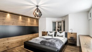 A modern bedroom with a wooden headboard, a bed with a black frame, a bedside table, and a nightstand. - Villa Tribulaunblick – Luxury Apartment with Fireplace, Terrace & Mountain View (Gossensass-Colle Isarco)