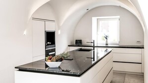 A modern kitchen with a large island, white cabinetry, and a built-in oven. - Villa Tribulaunblick – Luxury Apartment with Fireplace, Terrace & Mountain View (Gossensass-Colle Isarco)
