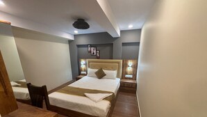 Una habitación de hotel con una cama grande, dos mesitas de noche, un escritorio de madera y una silla.