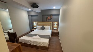 Una habitación de hotel moderna con una cama grande, cabecero de madera, lámparas de noche y un espejo.