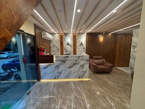 A reception area with a marble counter, wooden paneling, and a plush chair. - Hotel  New Zara Grand (Mumbai)
