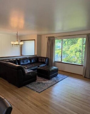 Relax in this inviting living room with a large sofa, ottoman, and a view of lush greenery outside.