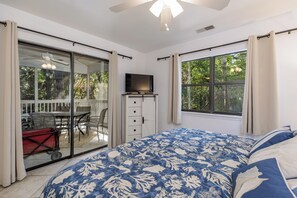 A bedroom with a large bed, a television on a stand, a sliding glass door leading to an outdoor patio, and a view of trees through the window.