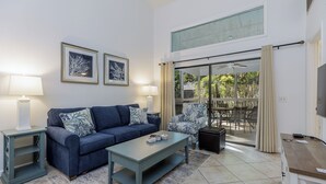 A living room with a sofa, coffee table, and a TV stand. There is a sliding glass door leading to an outdoor area.