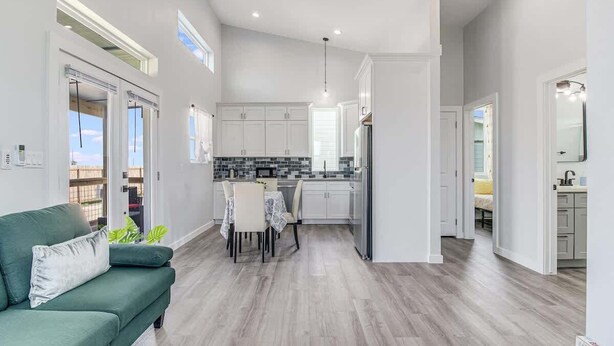 A modern kitchen with white cabinets, a dining area with a table and chairs, and a green sofa. - The Blue Flower (Rockport)