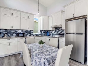 Una cocina moderna con armarios blancos, un refrigerador de acero inoxidable y una mesa de comedor con sillas.