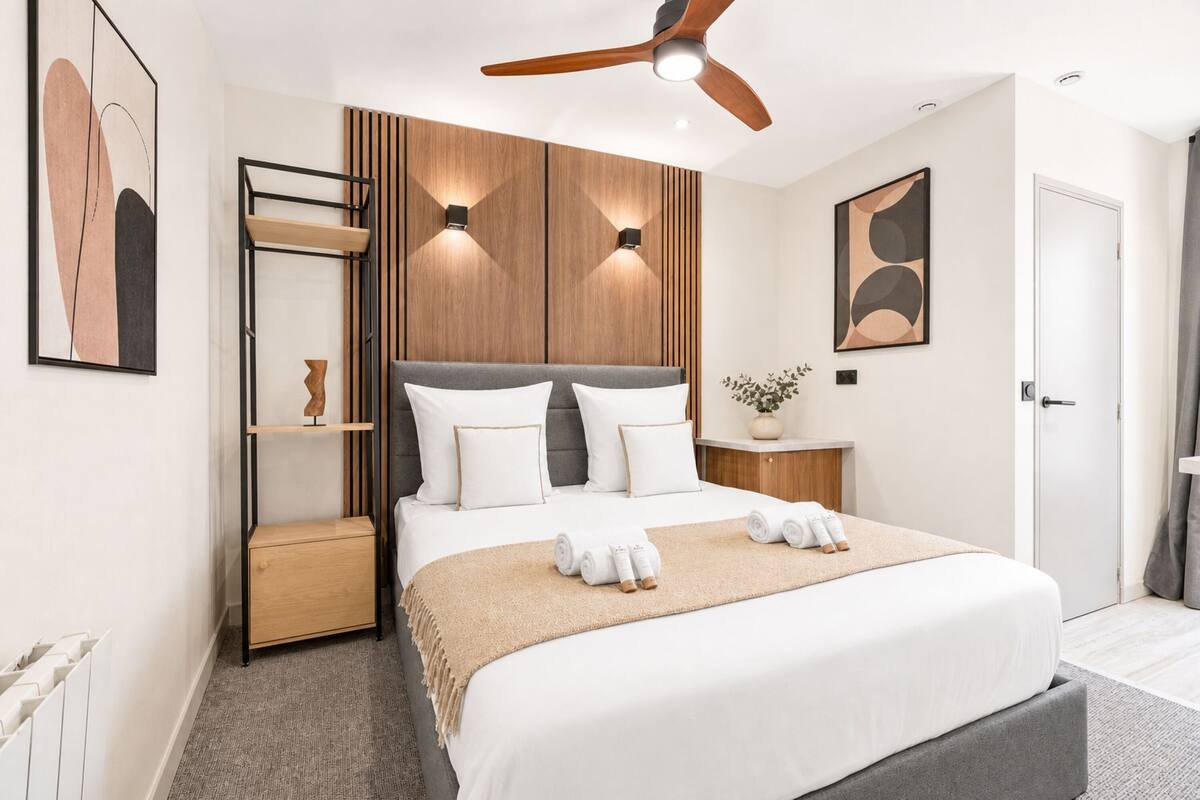 A modern bedroom with a bed, a ceiling fan, a bedside table, and a wall-mounted shelf.