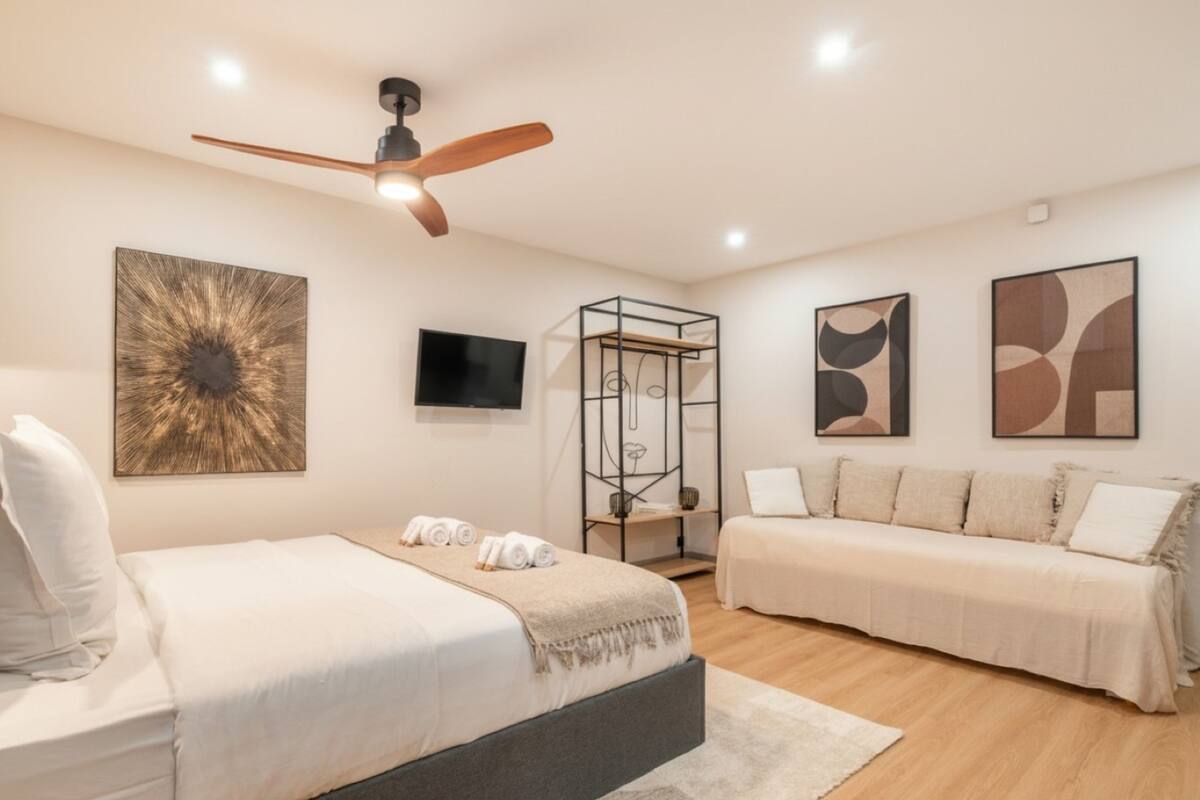 A modern bedroom with a bed, a sofa, a TV, and artwork on the walls.