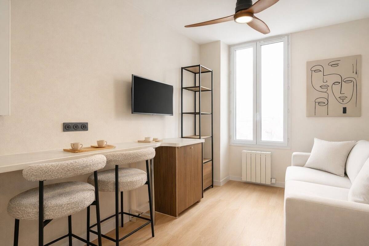 A modern kitchen with a bar area, a TV, a radiator, and a white sofa.