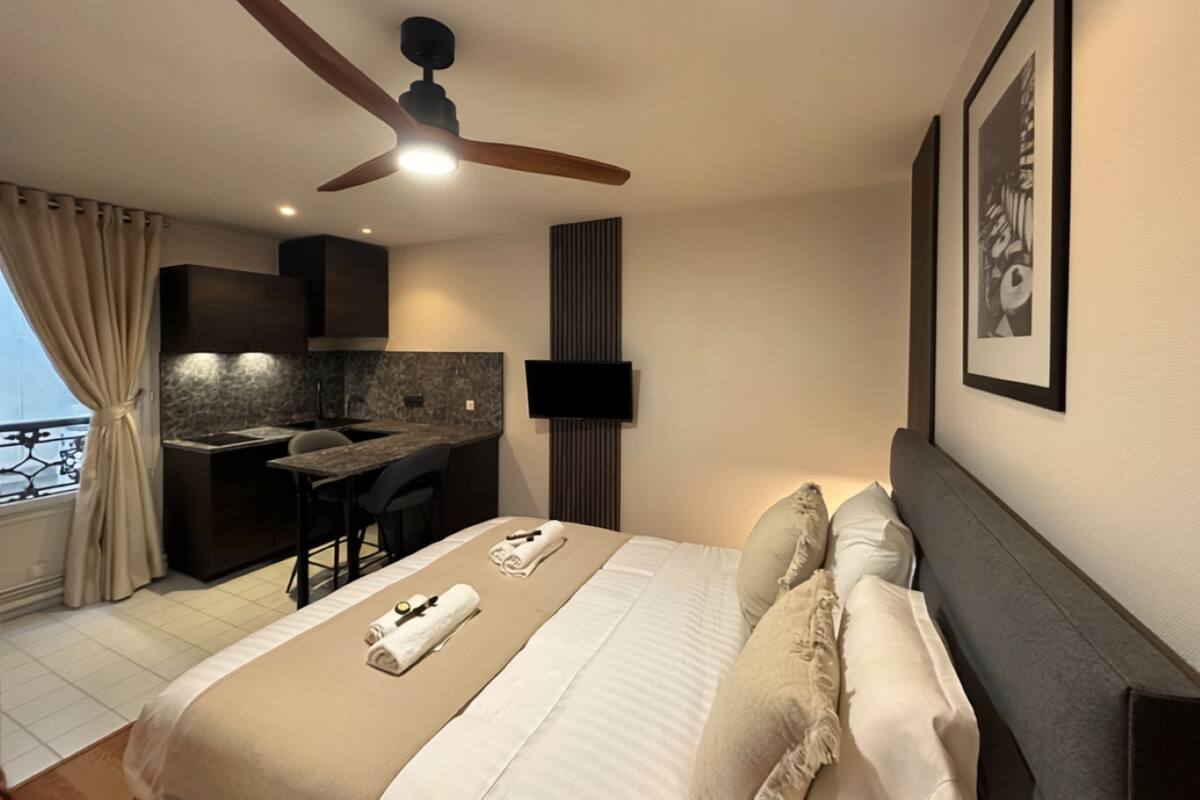 A modern hotel room with a bed, a desk, a ceiling fan, a TV, and a balcony view.