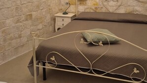 A bedroom with a stone wall, a bed with a metal frame, a nightstand, and a small table.