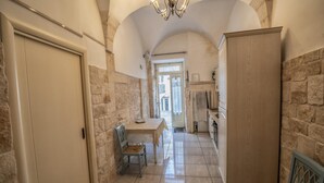 A narrow hallway with stone walls, a tiled floor, a wooden cabinet, a table with a chair, and a door.