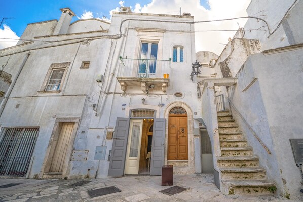 A historic building with a central wooden door, a balcony, and a staircase leading to an upper level.