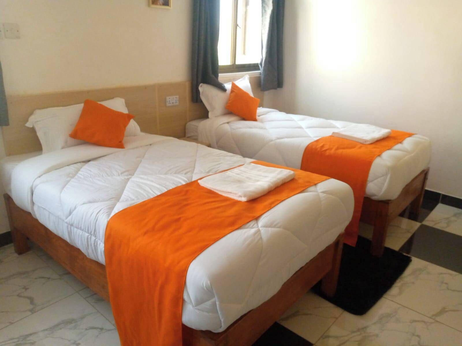 Two single beds with white and orange bedding, a window with curtains, and a checkered floor.