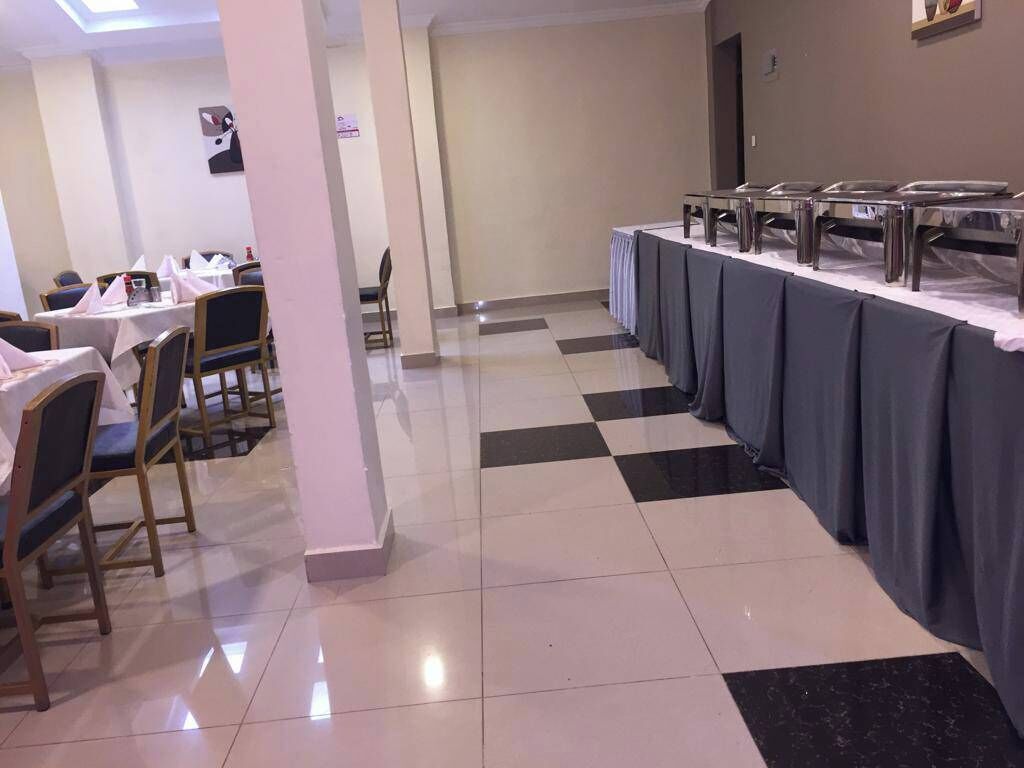 Uma sala de jantar de hotel com mesas, cadeiras, piso xadrez e um buffet.