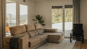 A modern living room with a beige sectional sofa, a black chair, and a large window with a view of greenery and hills. - Villa Cantinho da Cavadinha (Burgo)